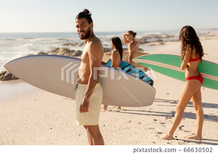 Mixed race people holding surf board on beach Mixed race people holding surf board on beach 66630502