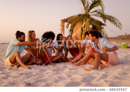 Multi-ethnic group of male and female sitting on the beach Multi-ethnic group of male and female sitting on the beach 66630567