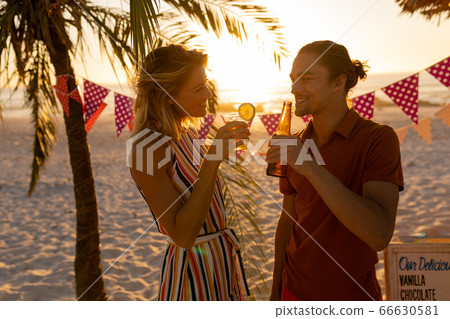 Caucasian couple smiling and drinking alcohol on beach Caucasian couple smiling and drinking alcohol on beach 66630581