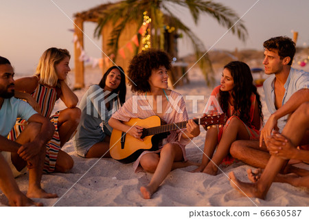 Multi-ethnic group of male and female sitting on the beach Multi-ethnic group of male and female sitting on the beach 66630587