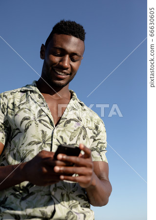 African american man using his phone on the beach African american man using his phone on the beach 66630605