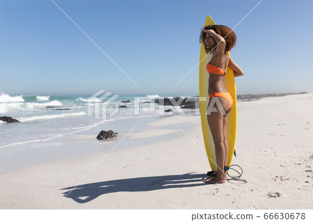 Mixed race woman holding a surfboard on the beach Mixed race woman holding a surfboard on the beach 66630678