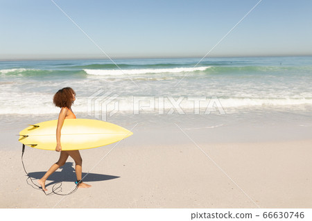 Mixed race woman holding a surfboard on the beach Mixed race woman holding a surfboard on the beach 66630746