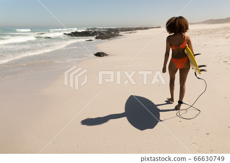 Mixed race woman holding a surfboard on the beach Mixed race woman holding a surfboard on the beach 66630749