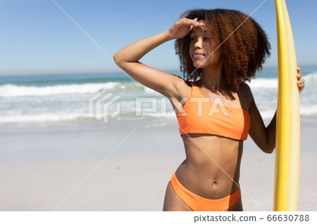 Mixed race woman holding a surfboard on the beach Mixed race woman holding a surfboard on the beach 66630788