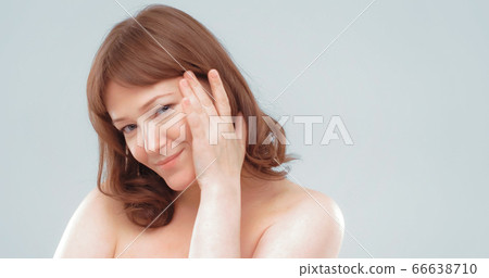 Naked smiling mature woman touches face with hand applying skin care product. Anti-aging skin care concept. Empty space for text at right side 66638710