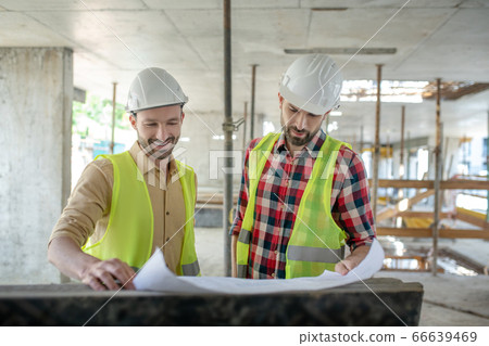 Building workers in yellow vests brainstorming over blueprint, discussing it, smiling 66639469