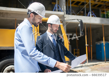 Building supervisor and foreman standing in front of building, studying carefully blueprint Building supervisor and foreman standing in front of building, studying carefully blueprint 66639517