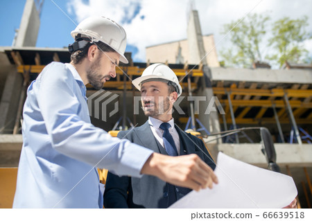 Building supervisor and foreman standing in front of building, discussing and checking blueprint Building supervisor and foreman standing in front of building, discussing and checking blueprint 66639518