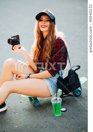 Hipster girl sitting on skateboard and taking 66640232