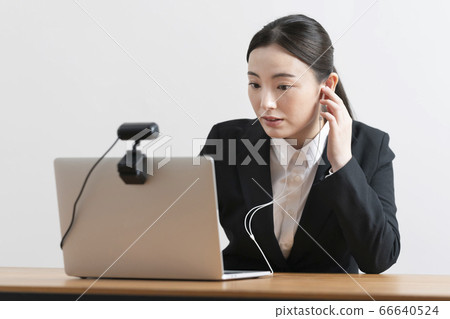 Online interview: A woman in a suit holding headphones while looking at the computer screen 66640524