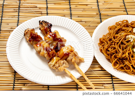 兩個烤雞肉串和蔥（去皮燒）放在紙碟上。在炒麵旁邊。夏季節日街頭食品菜單圖像。 66641044