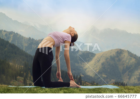 Yoga - outdoors young woman doing camel pose Ustrasana asana exercise outdoors in mountains in the morning 66645777