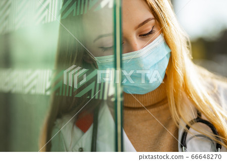 Close view of sad female doctor or nurse in surgical mask and white medical gown looking away Close view of sad female doctor or nurse in surgical mask and white medical gown looking away 66648270