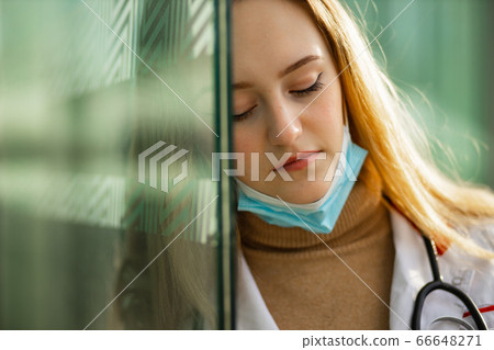Close view of sad female doctor or nurse in white medical gown taking off surgical mask Close view of sad female doctor or nurse in white medical gown taking off surgical mask 66648271