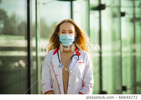 Female medical doctor or nurse in surgical mask and white medical gown looking at you Female medical doctor or nurse in surgical mask and white medical gown looking at you 66648272