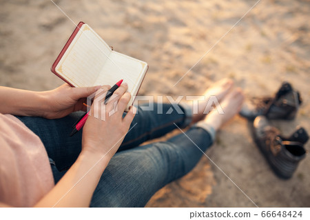 female makes notes and sitting on the beach; 66648424