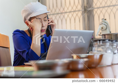 Serious woman baker talking on cell phone with laptop and bakery ingredient on table. 66649492