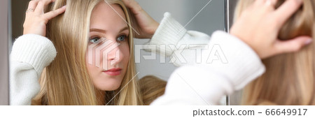 Girl looks mirror at reflection, straightens hair Girl looks mirror at reflection, straightens hair 66649917