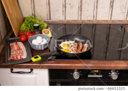 Frying pan with fried eggs and bacon on stove with fresh fruit and vegs near by 66652325