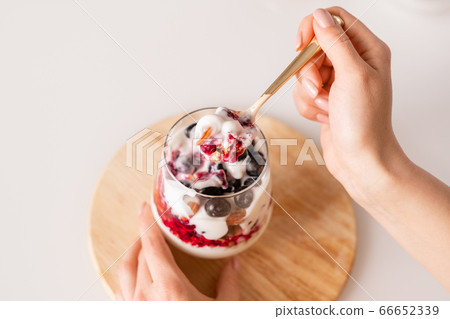 Hand of girl with teaspoon of fresh appetizing homemade yoghurt over glass Hand of girl with teaspoon of fresh appetizing homemade yoghurt over glass 66652339