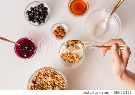 Hand of young woman with teaspoon putting muesli into glass with fresh sourcream Hand of young woman with teaspoon putting muesli into glass with fresh sourcream 66652351
