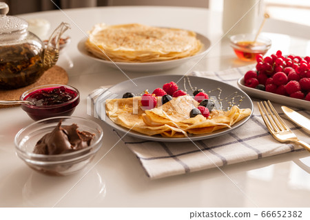 Appetizing crepes with berries and honey, bowls with jam and chocolate cream 66652382