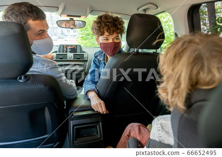 Young parents in protective masks looking at their cute little son on backseat Young parents in protective masks looking at their cute little son on backseat 66652495