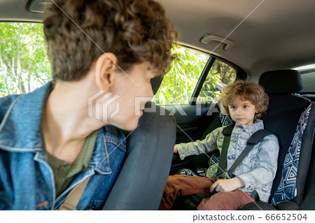 Cute little boy on backseat of car looking at his mother sitting in front of him 66652504