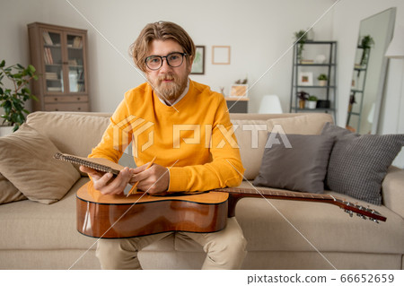 Young successful music teacher in casualwear sitting on couch and making notes Young successful music teacher in casualwear sitting on couch and making notes 66652659