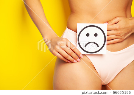 Woman health problem and menstruation pain, closeup of woman's hands holding a sad smile card near her belly 66655196