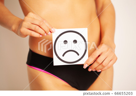 Woman health problem and menstruation pain, closeup of woman's hands holding a sad smile card near her belly 66655203