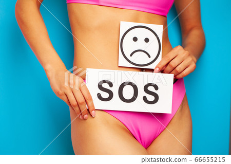 Woman health problem and menstruation pain, closeup of woman's hands holding a sad smile card near her belly 66655215