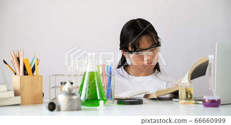 Young adorable school girl reading a chemistry book while doing a scientific experiment. 66660999