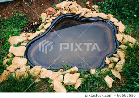 Beautiful pond in a backyard surrounded with stone during summer Beautiful pond in a backyard surrounded with stone during summer 66663686