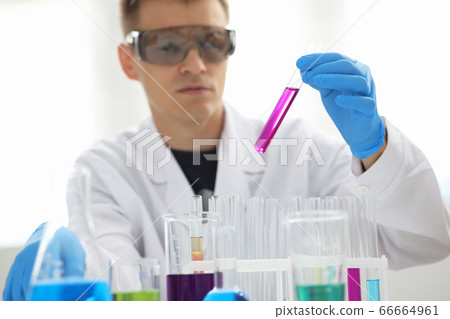 A male chemist holds test tube of glass in his hand overflows a liquid solution A male chemist holds test tube of glass in his hand overflows a liquid solution 66664961