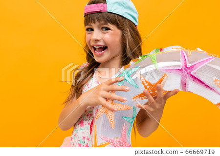 Beautiful little girl in swinsuit holds a rubber ring isolated on yellow and orange background 66669719