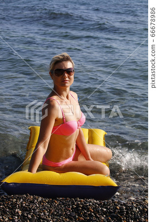 Happy woman in sunglasses sitting on air mattress by the sea 66678986