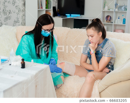 A teenage girl with a knee injury at a trauma doctor's appointment, for bandaging abrasions. 66683205