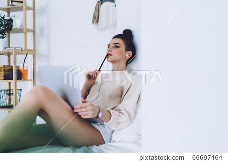 Pensive woman sitting on bed with computer Pensive woman sitting on bed with computer 66697464