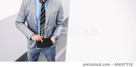 Smart male professional worker using touch pad while standing in office space Smart male professional worker using touch pad while standing in office space 66697558