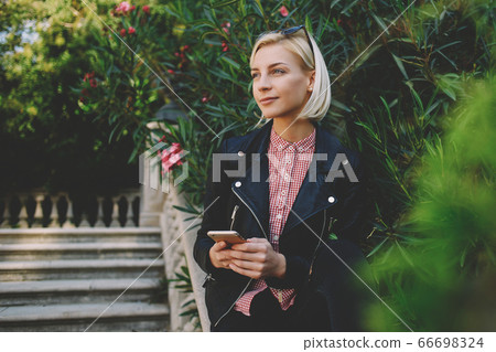 pretty female is reading text message on her cell telephone while relaxing in the park 66698324