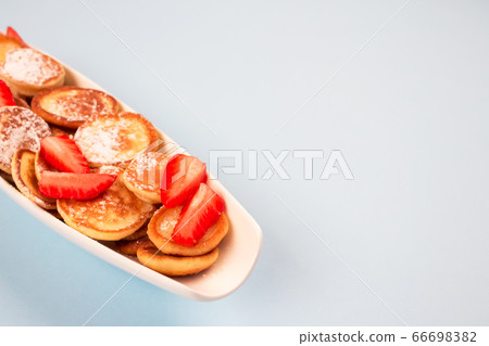 Close up of mini pancakes cereal with strawberries on white plate on blue background with copy space for recipe or your text. Breakfast concept, trendy food 66698382