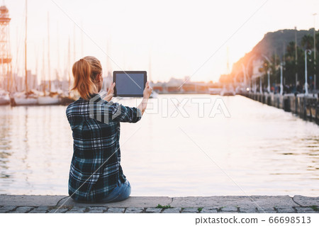 Young gorgeous woman using touch pad while sitting against sea port background with copy space 66698513