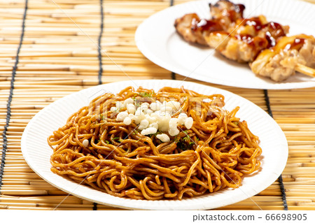 Sauce fried noodles on a paper plate. There is also a yakitori in the back of the photo. Summer festival street food menu image. Sauce fried noodles on a paper plate. There is also a yakitori in the back of the photo. Summer festival street food menu image. 66698905