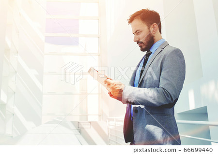 Half length portrait of rich businessman holding portable digital tablet during work break in hallway Half length portrait of rich businessman holding portable digital tablet during work break in hallway 66699440