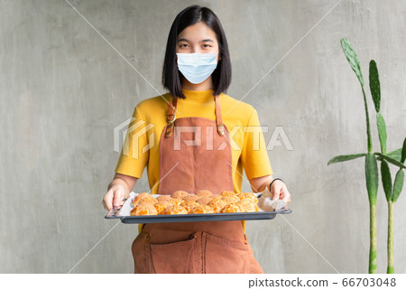Woman in medical mask holding baking tray with choux cream SME concept. 66703048