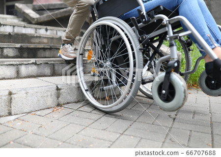 Social worker helps disabled person in wheelchair climb stairs 66707688