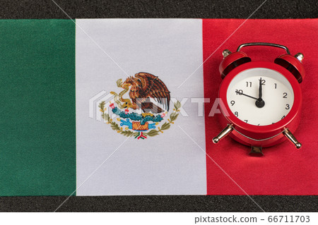 Mexico flag and vintage alarm clock close up. Time 66711703