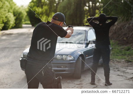 The policeman is targeting an offender near the stolen car. Stop criminality. The policeman is targeting an offender near the stolen car. Stop criminality. 66712271